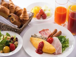 A breakfast setting with croissants, a fruit salad, ham, eggs, and juice.
