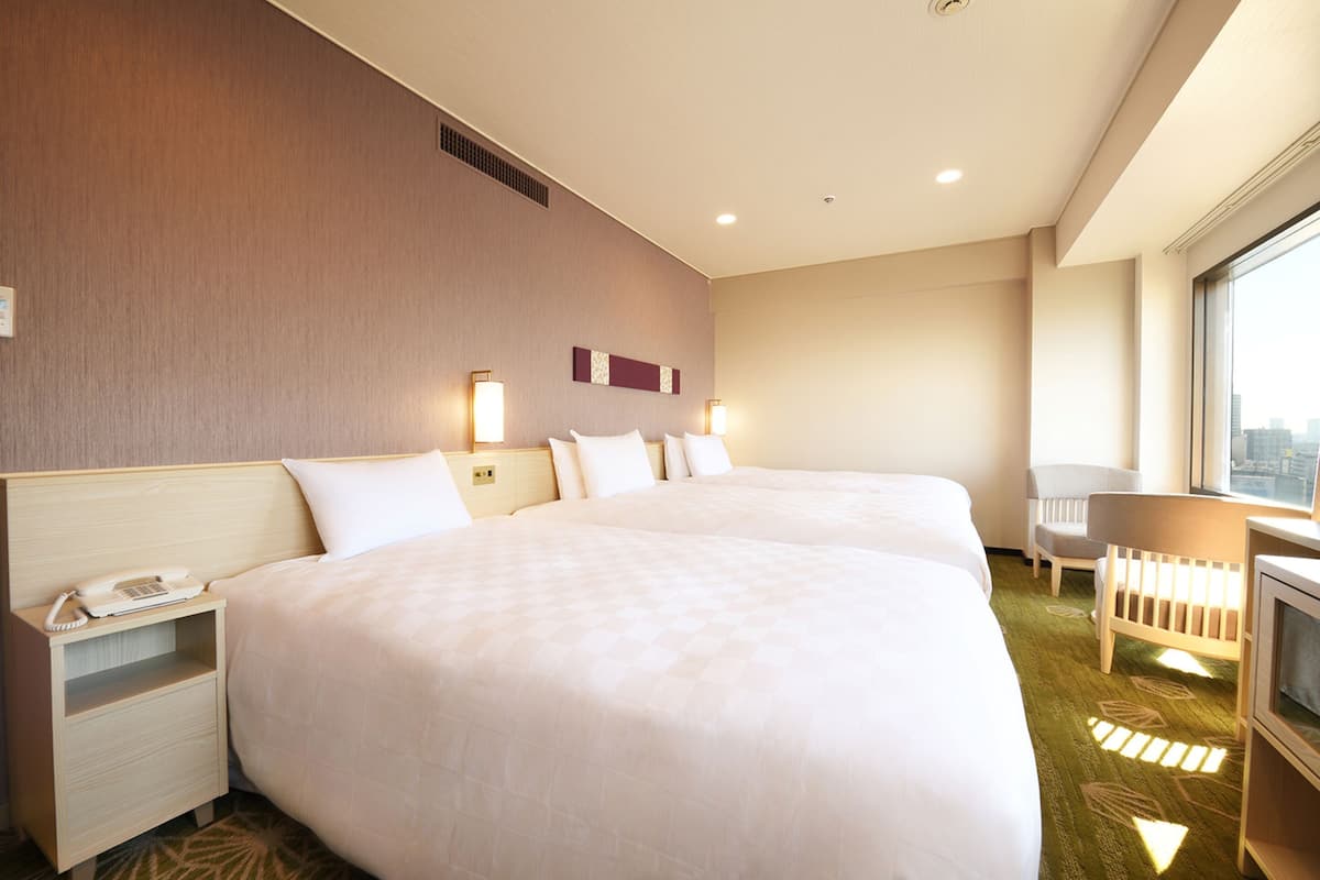 A hotel room with two beds, a desk, a chair, and a TV.