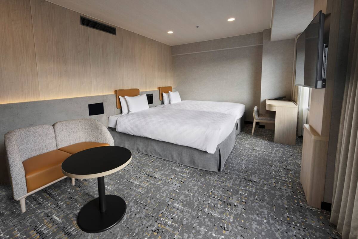 A modern hotel room with a large bed, a sofa, a small table, and a TV.