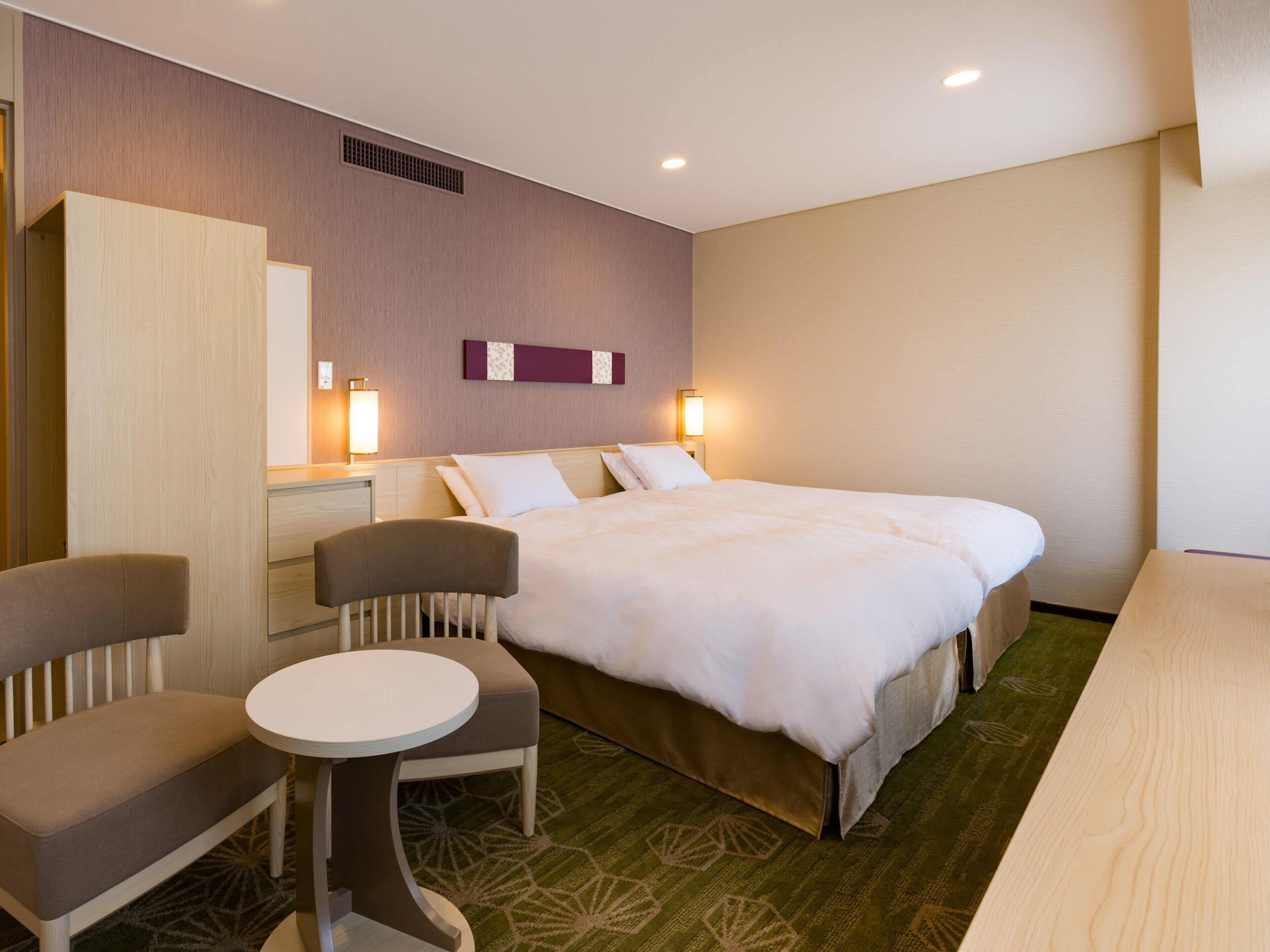 A hotel room with a bed, a desk, a chair, and a small table.
