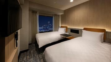 A hotel room with two beds, a TV, a desk, and a view of the cityscape at night.