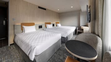 A hotel room with two beds, a small table, a chair, and a TV mounted on the wall.