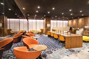 A modern hotel lobby with a reception desk, seating area, and large windows.