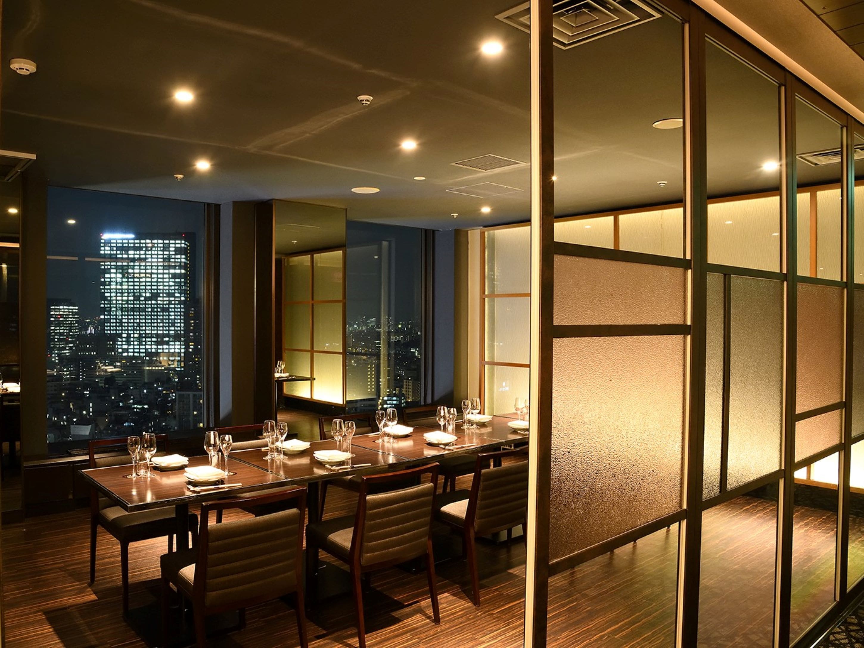 A dining area with a city view, a long table set for four, and traditional sliding doors.