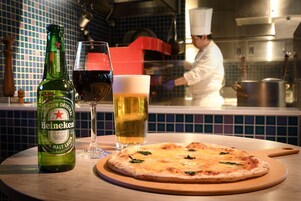 A Heineken beer bottle, a glass of red wine, and a beer glass on a table with a pizza.