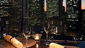 A table set for two with wine glasses and a candle, overlooking a cityscape at dusk.