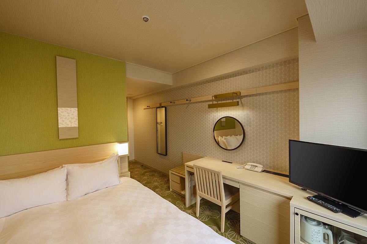 A hotel room with a bed, desk, chair, television, and a mirror.