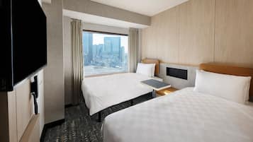 A hotel room with two beds, a TV, a small table, and a view of the city.