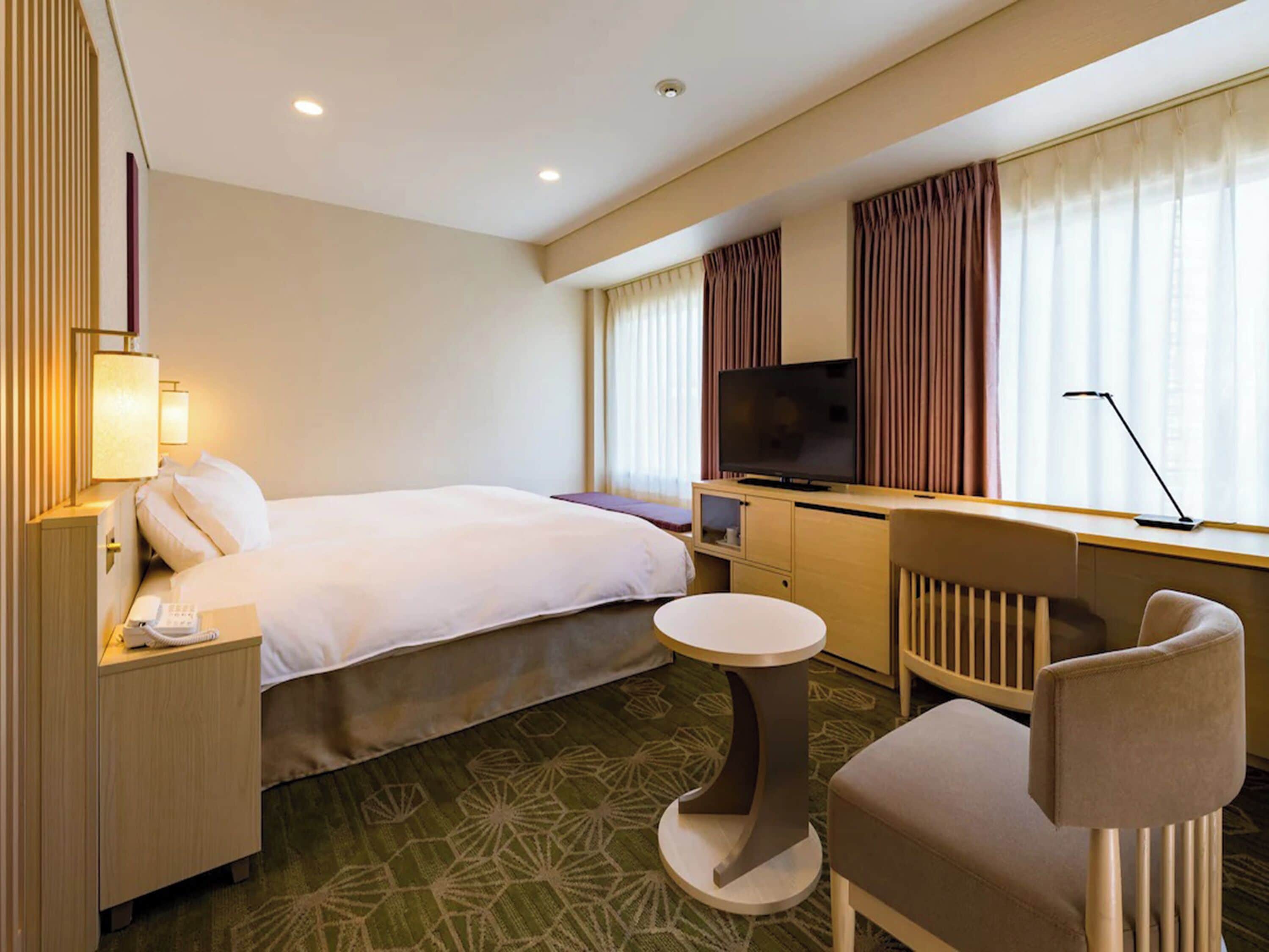 Habitación de hotel con cama, escritorio con televisor, una silla y una mesita.
