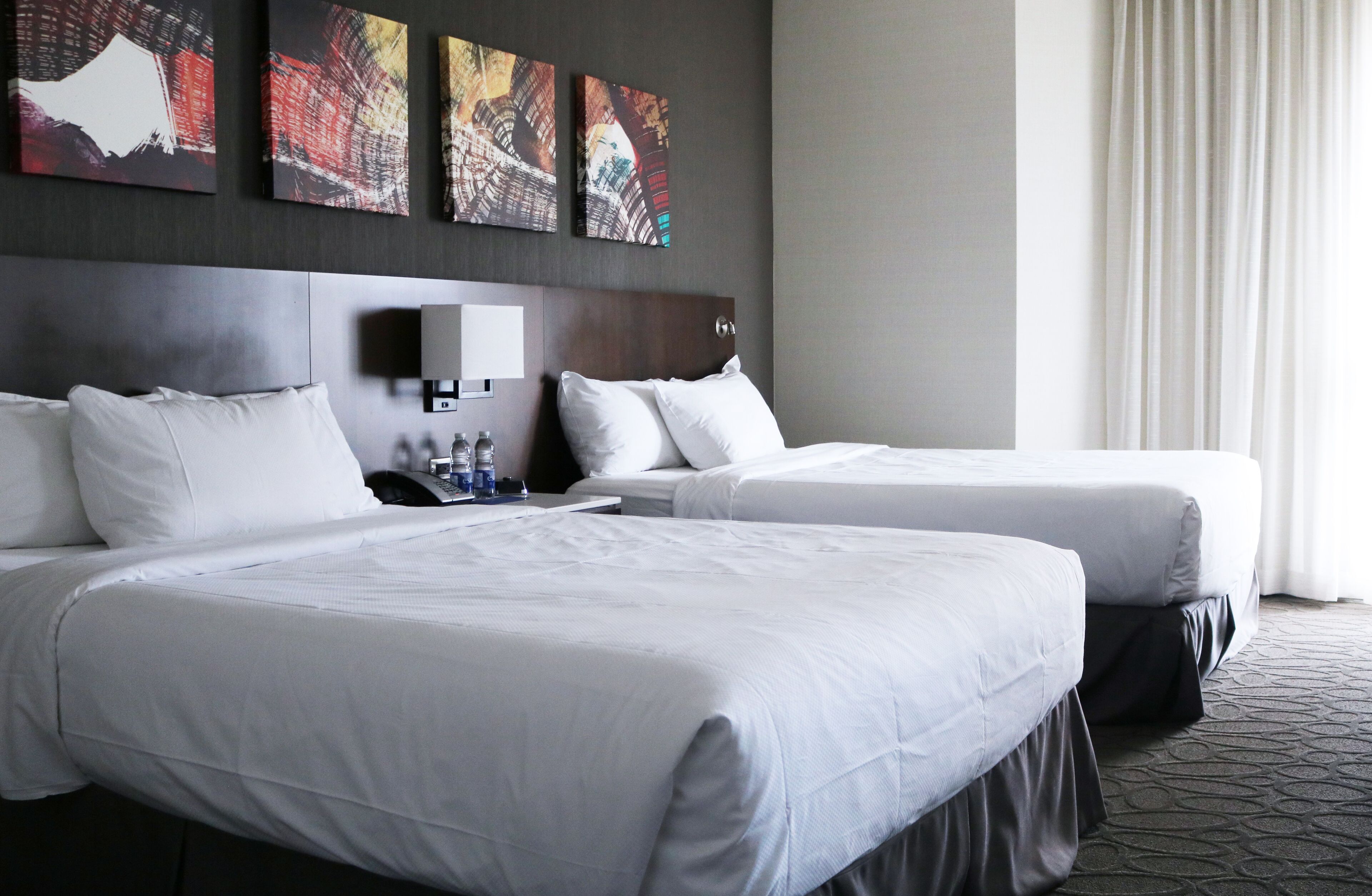 A hotel room with two beds, a nightstand, a lamp, and three wall-mounted artworks.