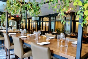 A restaurant with long wooden tables, beige chairs, and hanging plants. - Delta Hotels by Marriott Montreal (Montreal)