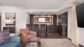 A hotel room with a seating area, a kitchenette, and a large mirror.