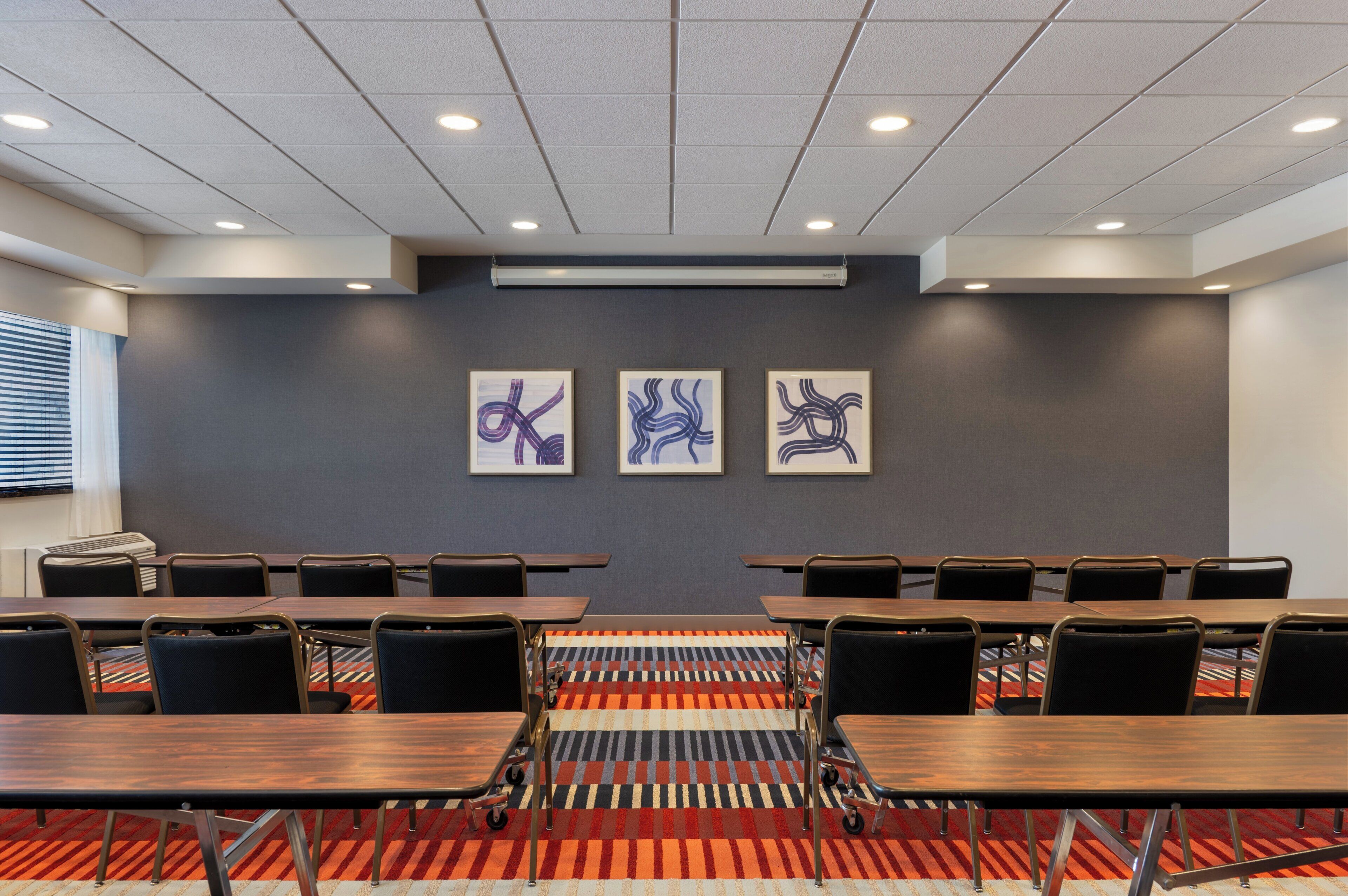 A conference room with a long table, chairs, and three abstract paintings on the wall.