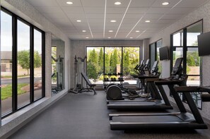 A gym with treadmills, weights, and exercise equipment, large windows, and a view of trees and a building.