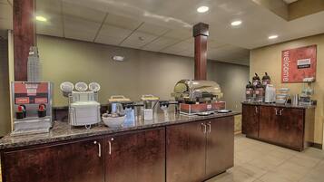 A breakfast bar with coffee machines, a griddle, and various food containers.