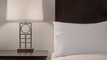 A neatly made bed with a white pillow and a dark wooden nightstand with a lamp.