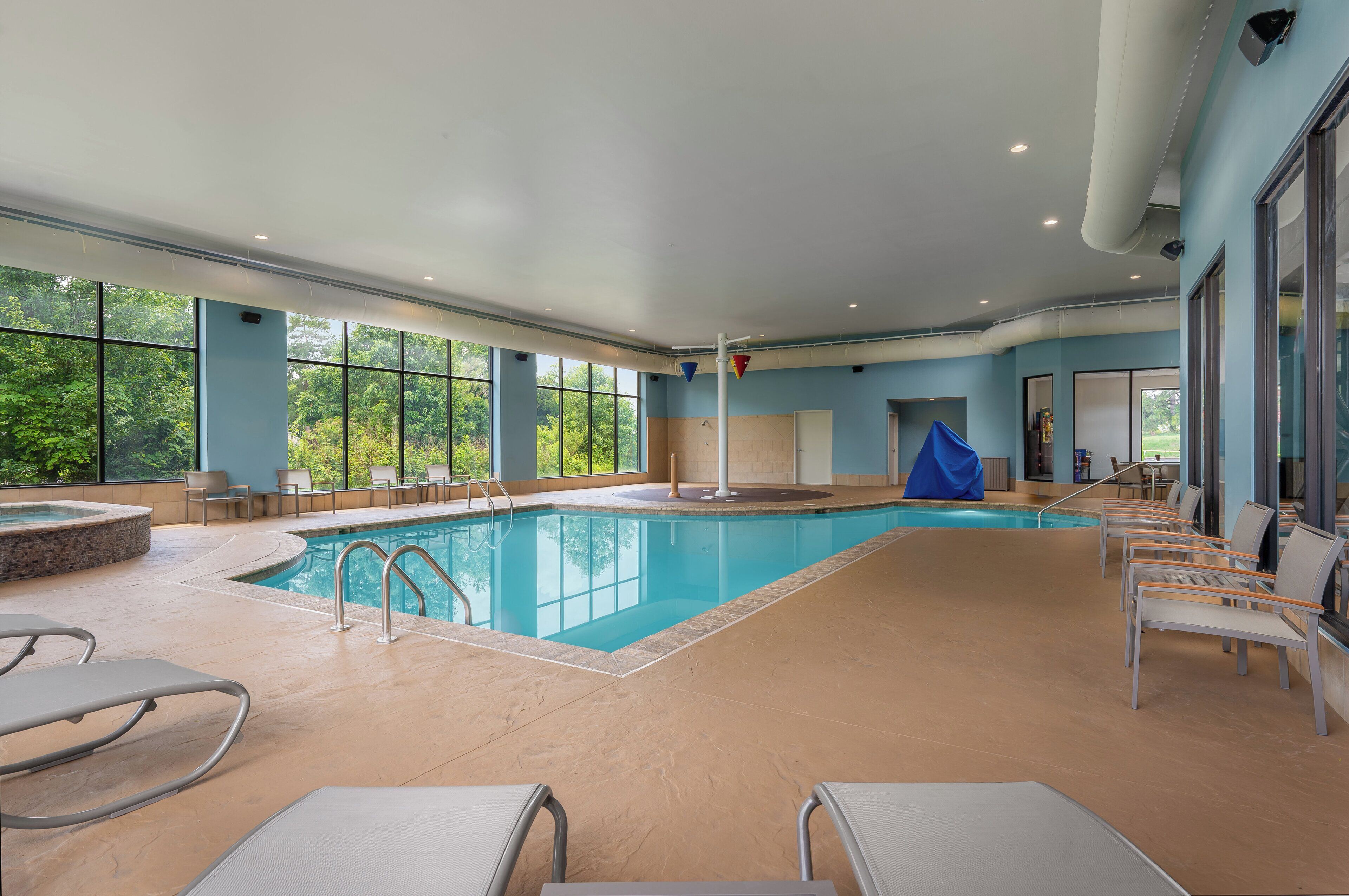 An indoor swimming pool with clear views of the outdoors, surrounded by seating and a covered area.