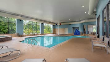 An indoor swimming pool with clear views of the outdoors, surrounded by seating and a covered area.
