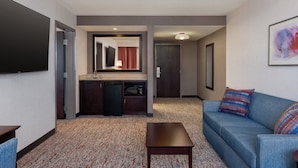 A hotel room with a kitchenette, a sofa, a coffee table, and a flat-screen TV.
