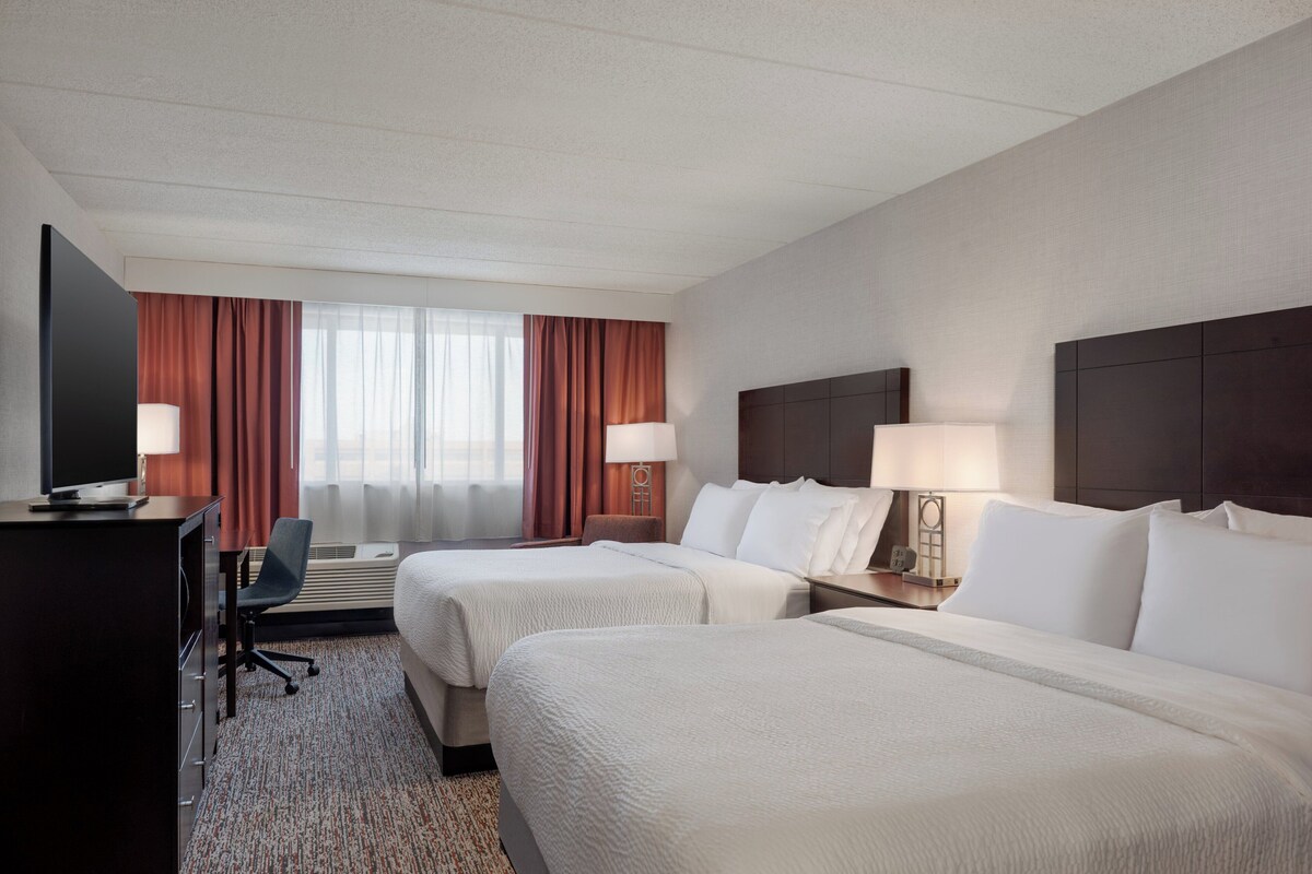 Une chambre d’hôtel avec deux lits, un bureau avec une télévision, une chaise et deux lampes de chevet.