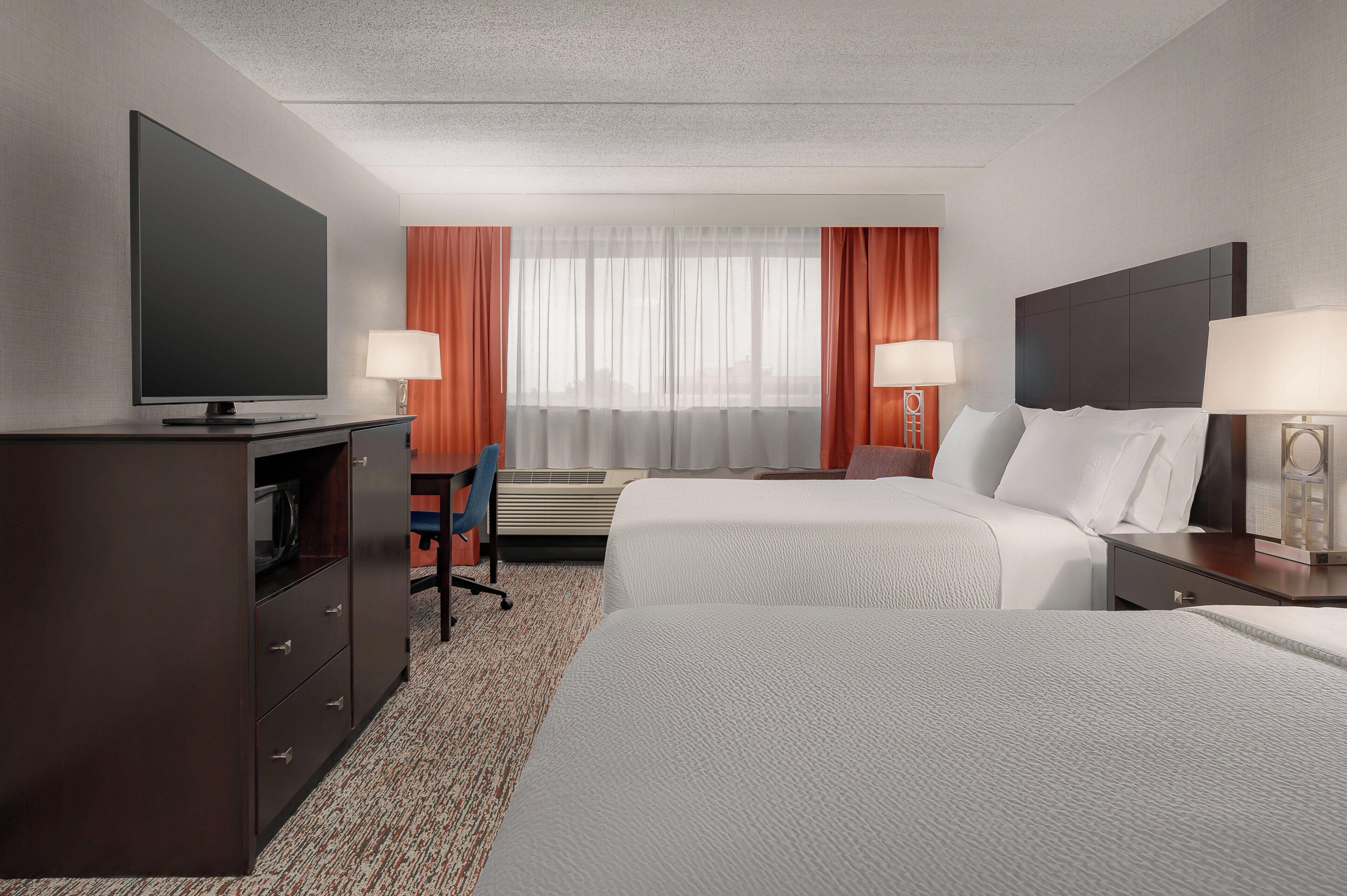 A hotel room with a bed, a desk, a television, and a window with curtains.
