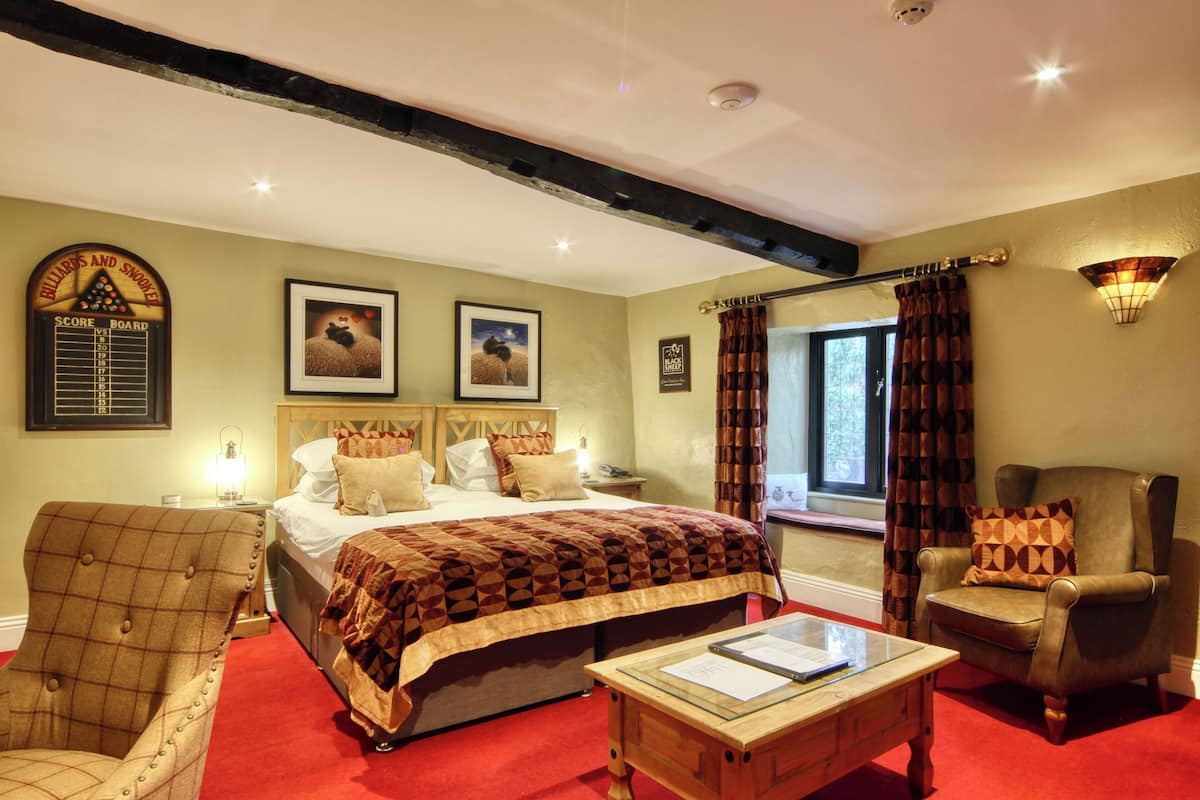 A hotel room with a large bed, a wooden chair, a small table, and a window with curtains.