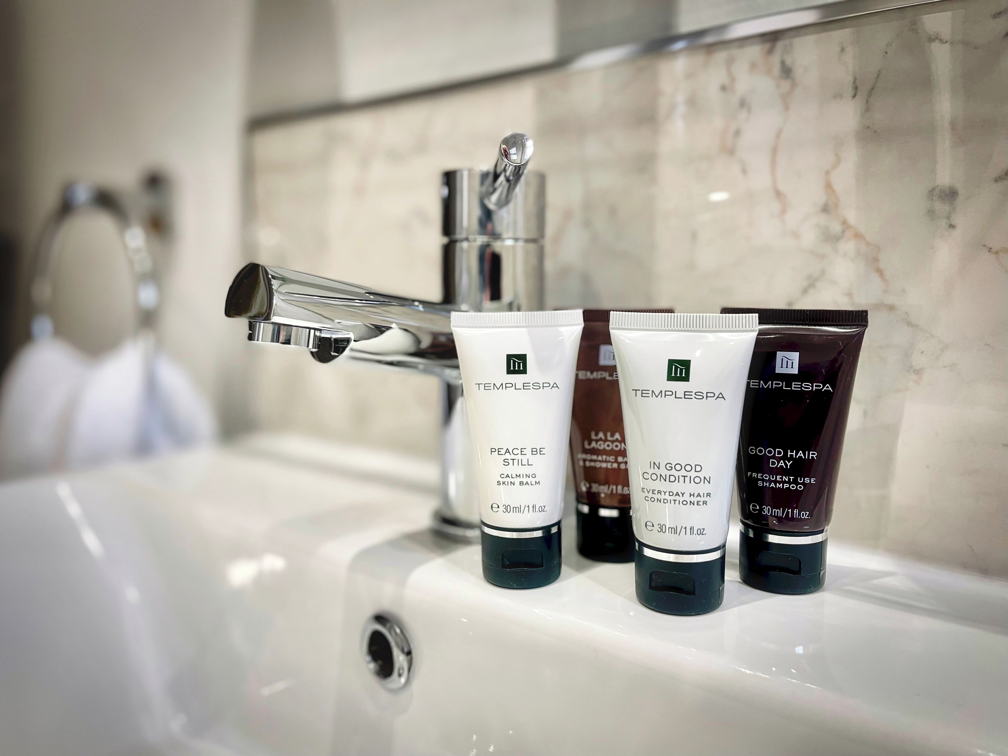 A bathroom sink with three toiletries: a skin balm, a hair conditioner, and a shampoo.