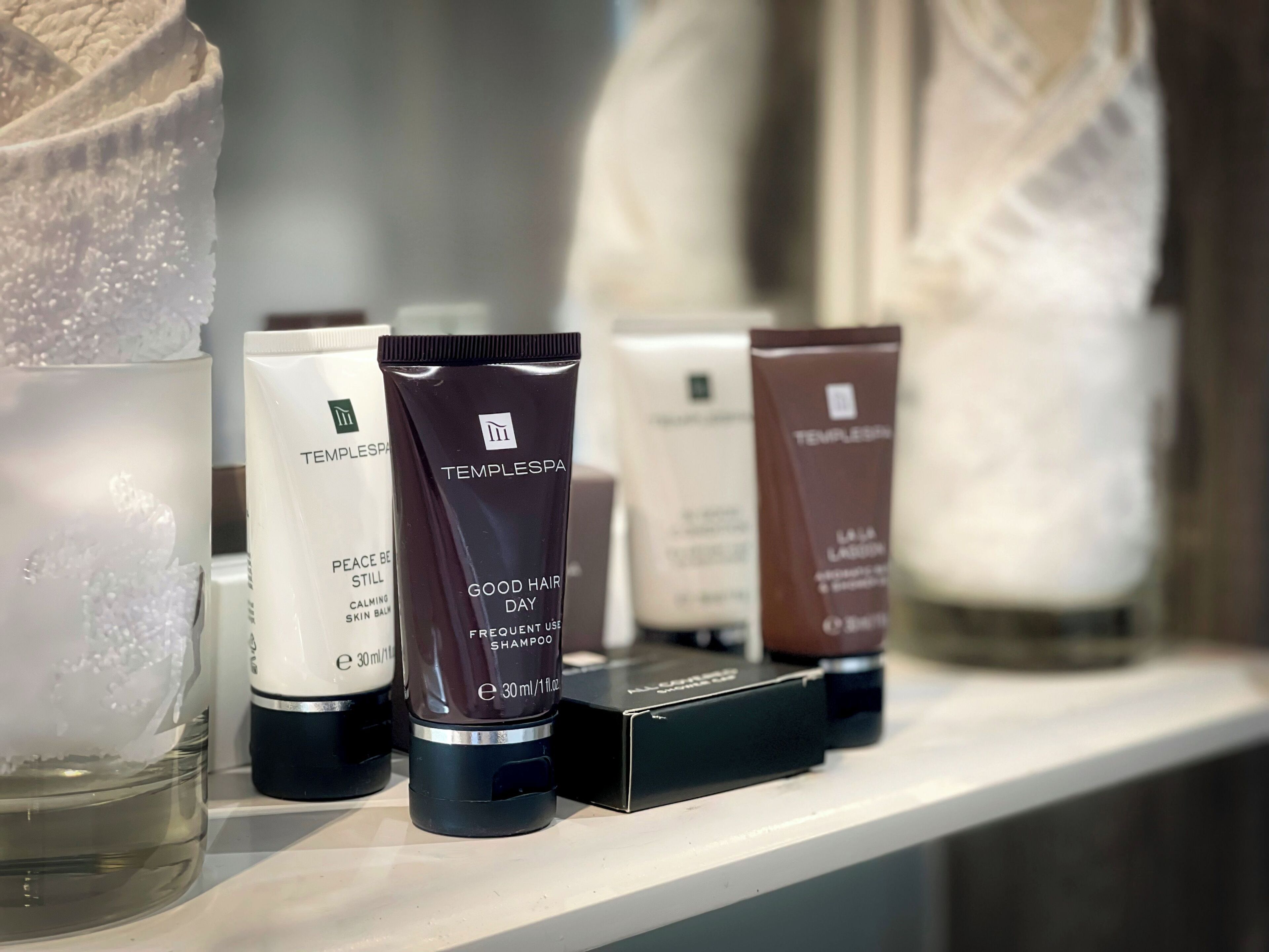 Una estantería con varios productos TempleSpa, incluyendo champú Good Hair Day y otros artículos de cuidado de la piel.