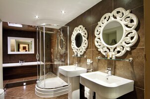 Un baño moderno con ducha de vidrio, dos lavamanos y espejos decorativos.