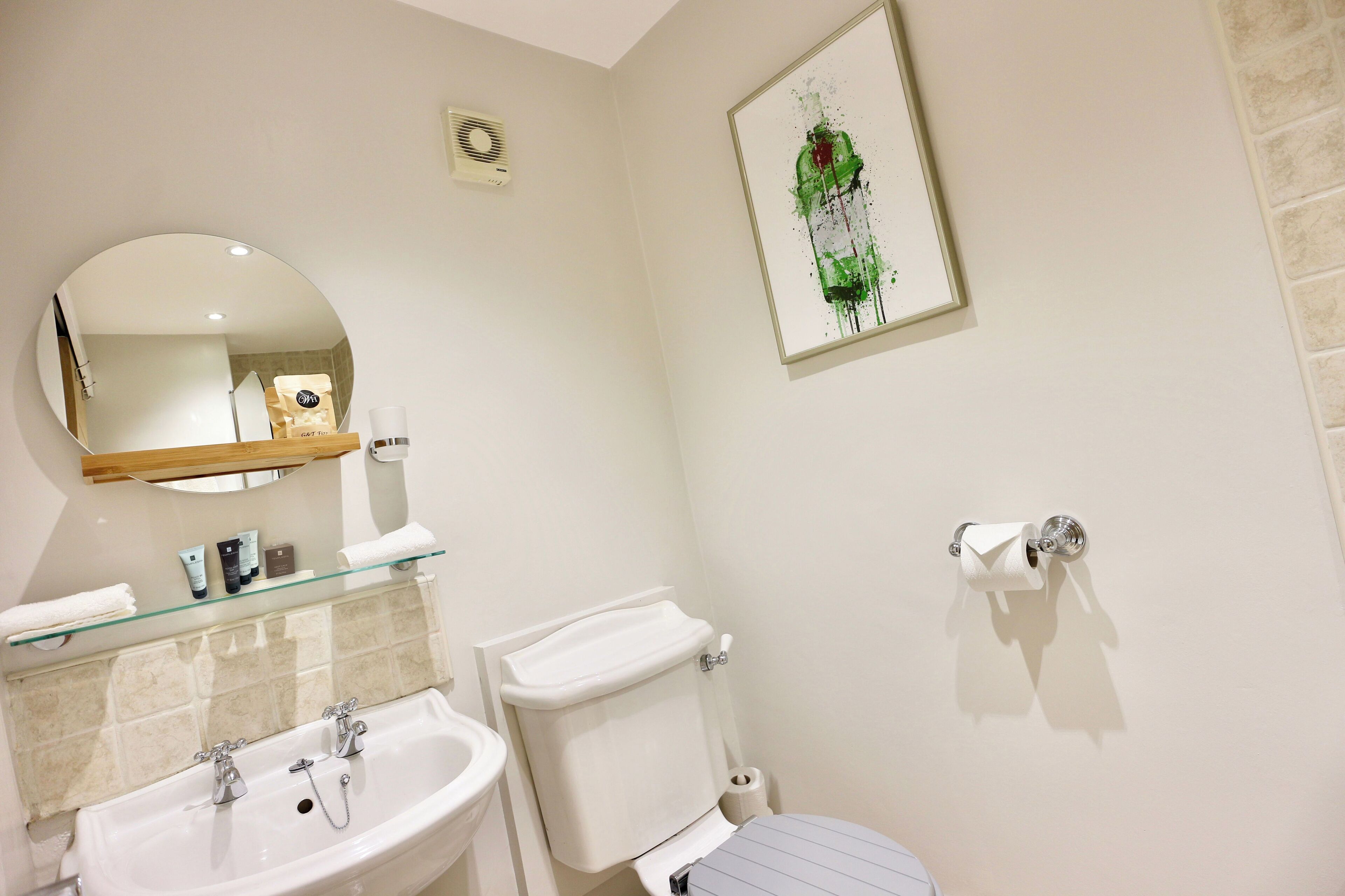Une salle de bain avec un lavabo, un miroir, des toilettes et une œuvre d’art encadrée accrochée au mur.
