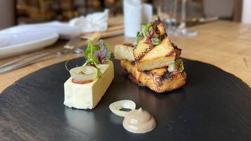 A black slate plate with two gourmet dishes, a glass of wine, and a napkin on a wooden table.