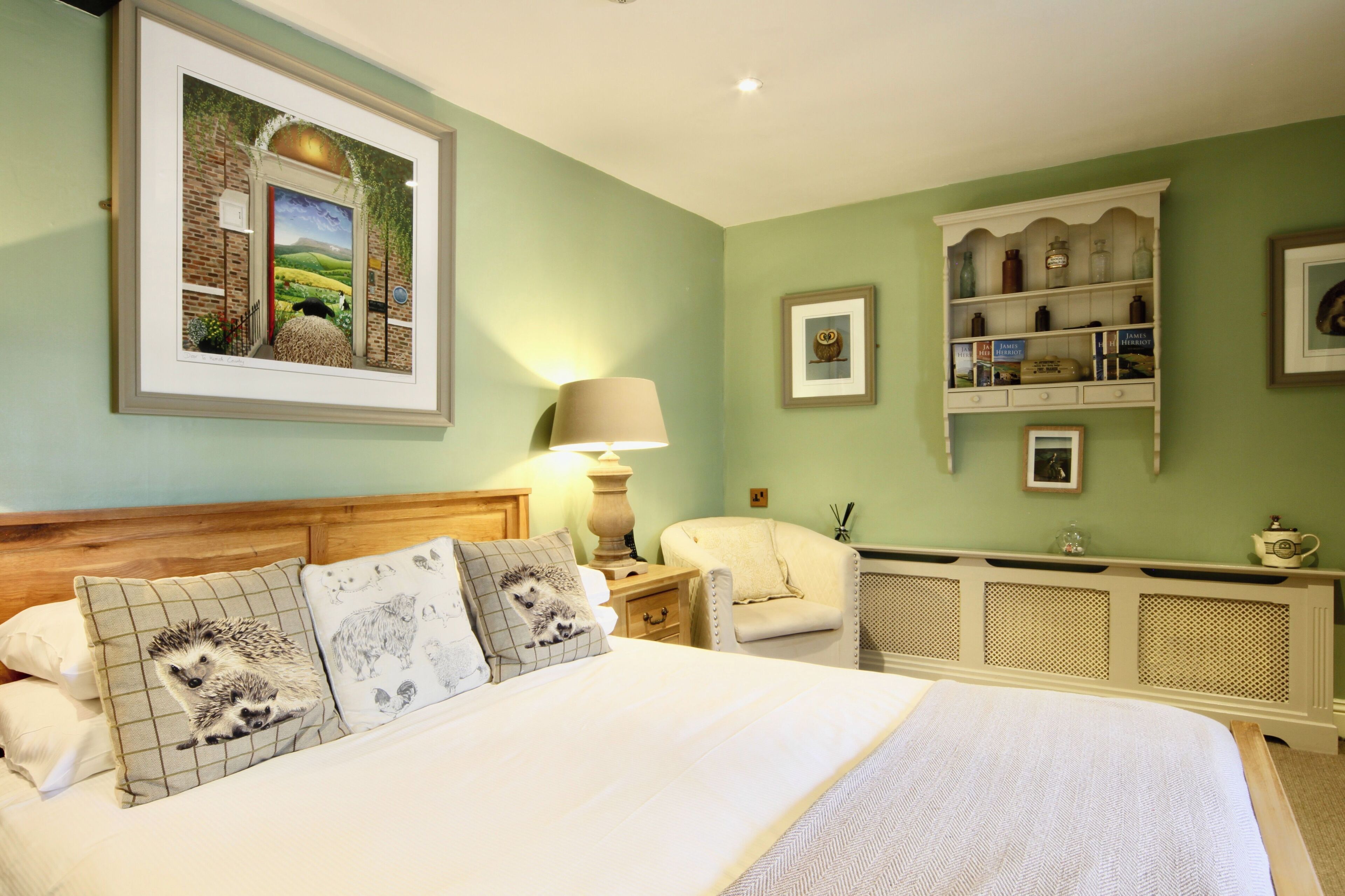 Une chambre à coucher avec un grand lit, une table de chevet avec une lampe, une chaise et une étagère ornée d’objets décoratifs.