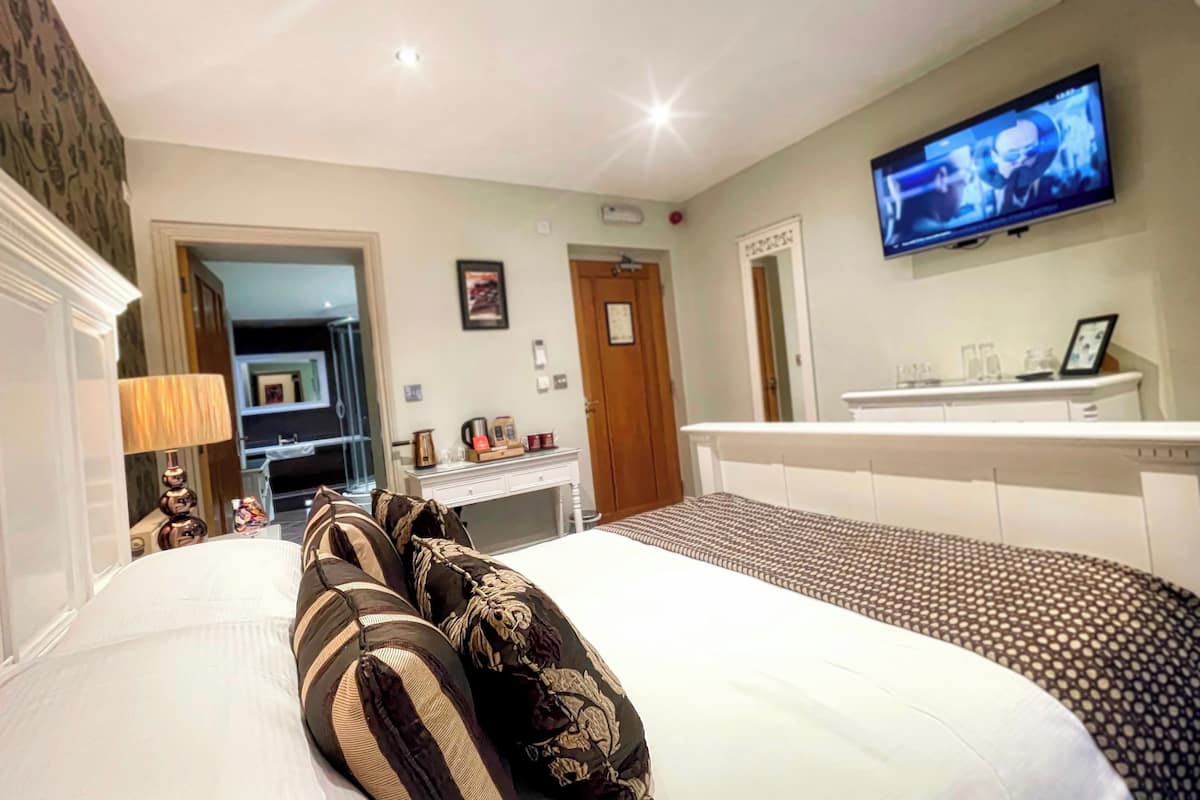 A hotel room with a bed, a desk, a television, and a bathroom visible through an open door.