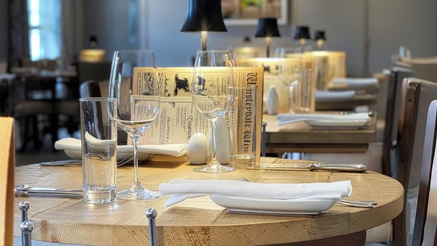 A dining table set with wine glasses, a bottle, and a menu. - The Wensleydale Heifer (Leyburn)