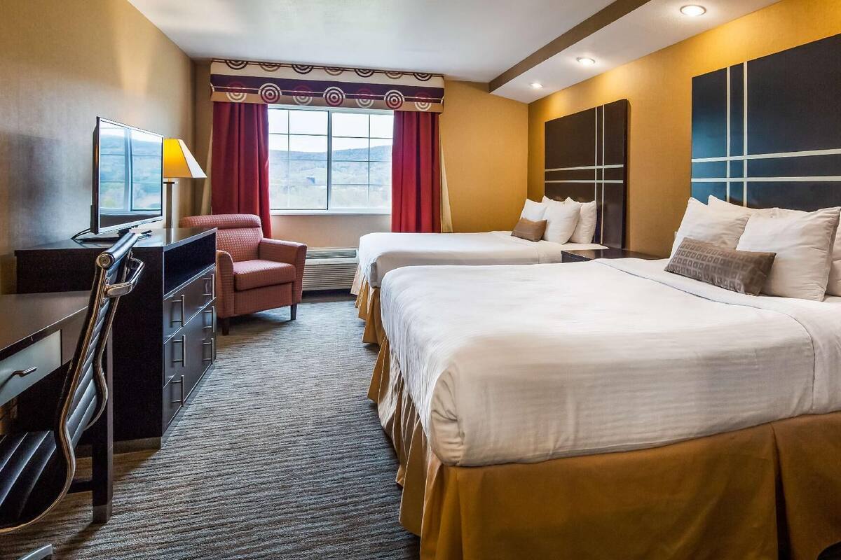 A hotel room with two beds, a desk with a computer, a chair, and a large window with curtains.