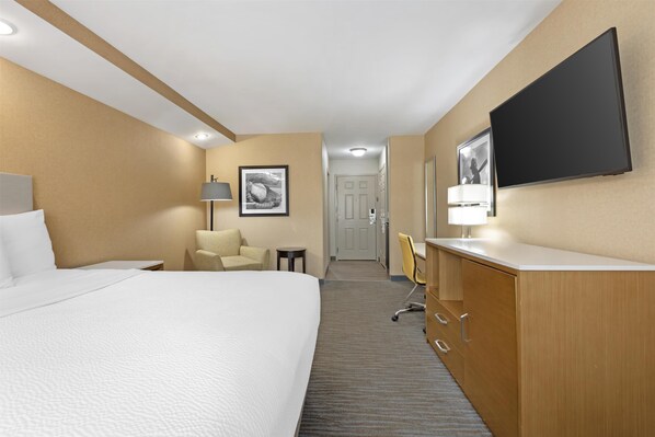 A hotel room with a large bed, a desk with a chair, a television mounted on the wall, and a door leading to another room.