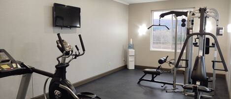 A gym with cardio equipment, weight machines, and a TV on the wall.
