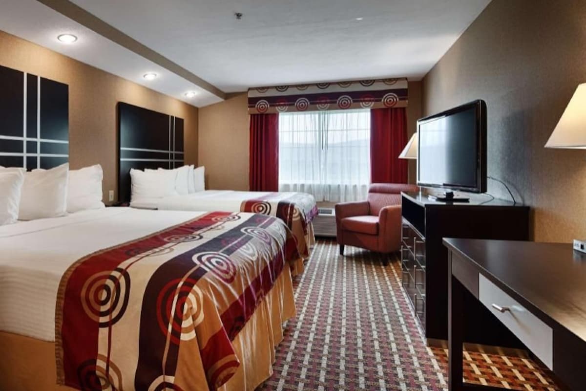 A hotel room with two beds, a desk, a TV, and a chair.