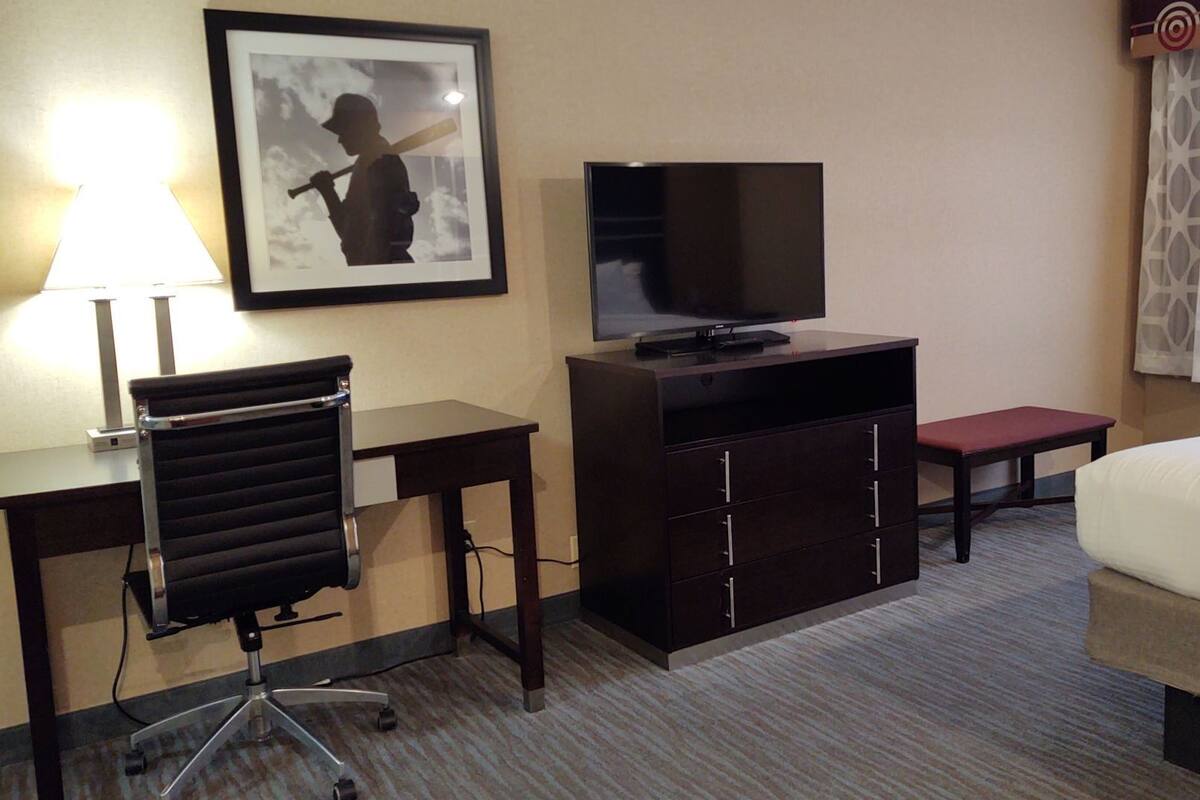 A hotel room with a bed, a desk with a chair, a television, a small table, and a picture on the wall.