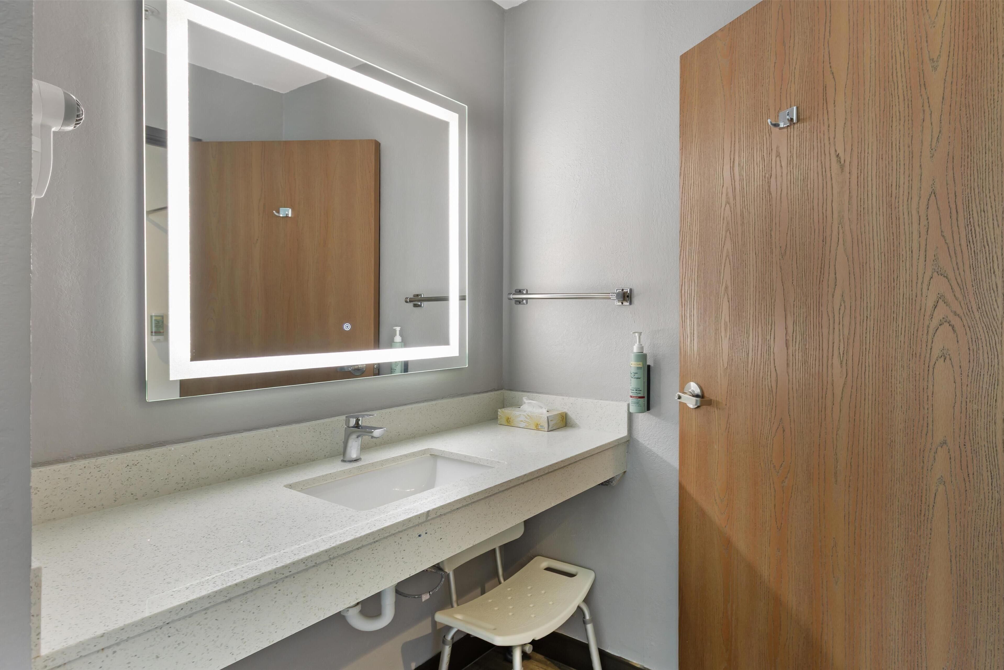 A modern bathroom with a large mirror, a sink, and a wooden door.