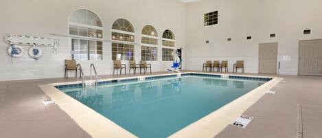 Una amplia piscina interior con varias pistas, rodeada de paredes color beige y grandes ventanales arqueados.