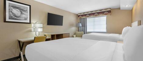Una habitación de hotel con una cama grande, un escritorio con silla, un televisor y un ventanal con cortinas.