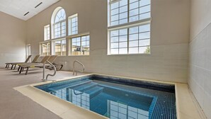 Une piscine intérieure à l’eau d’un bleu cristallin, entourée de murs de couleur beige et dotée de grandes fenêtres.
