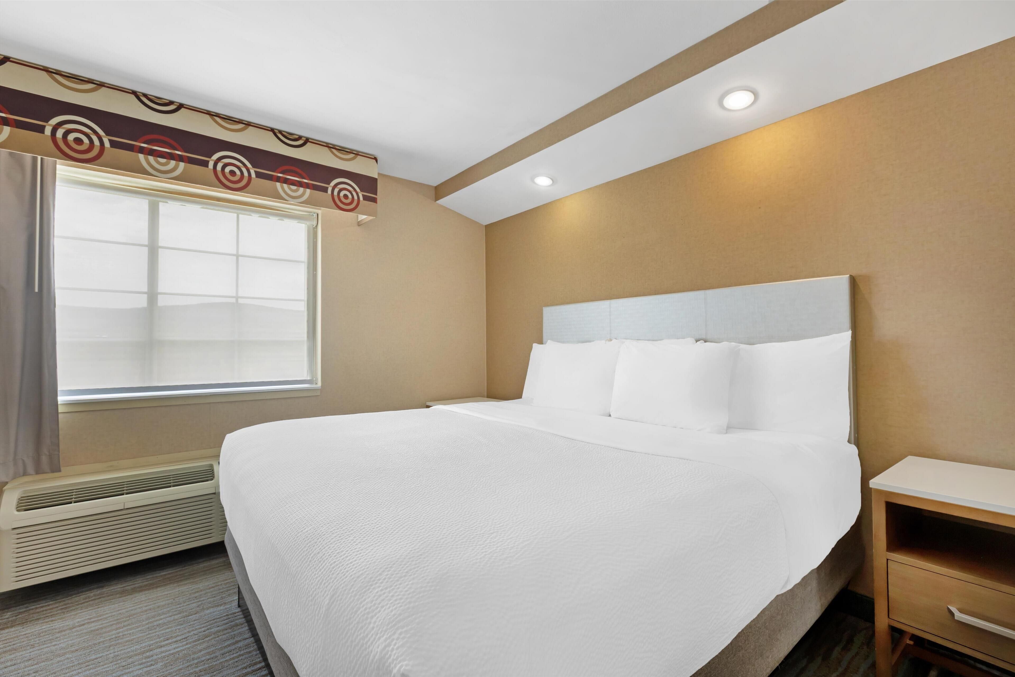 Een hotelkamer met een groot bed, nachtkastje, verwarming en een raam met gordijnen.
