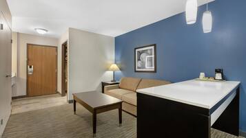 Une chambre d’hôtel équipée d’une kitchenette, d’un canapé, d’une table basse, d’une lampe et d’un tableau encadré au mur.
