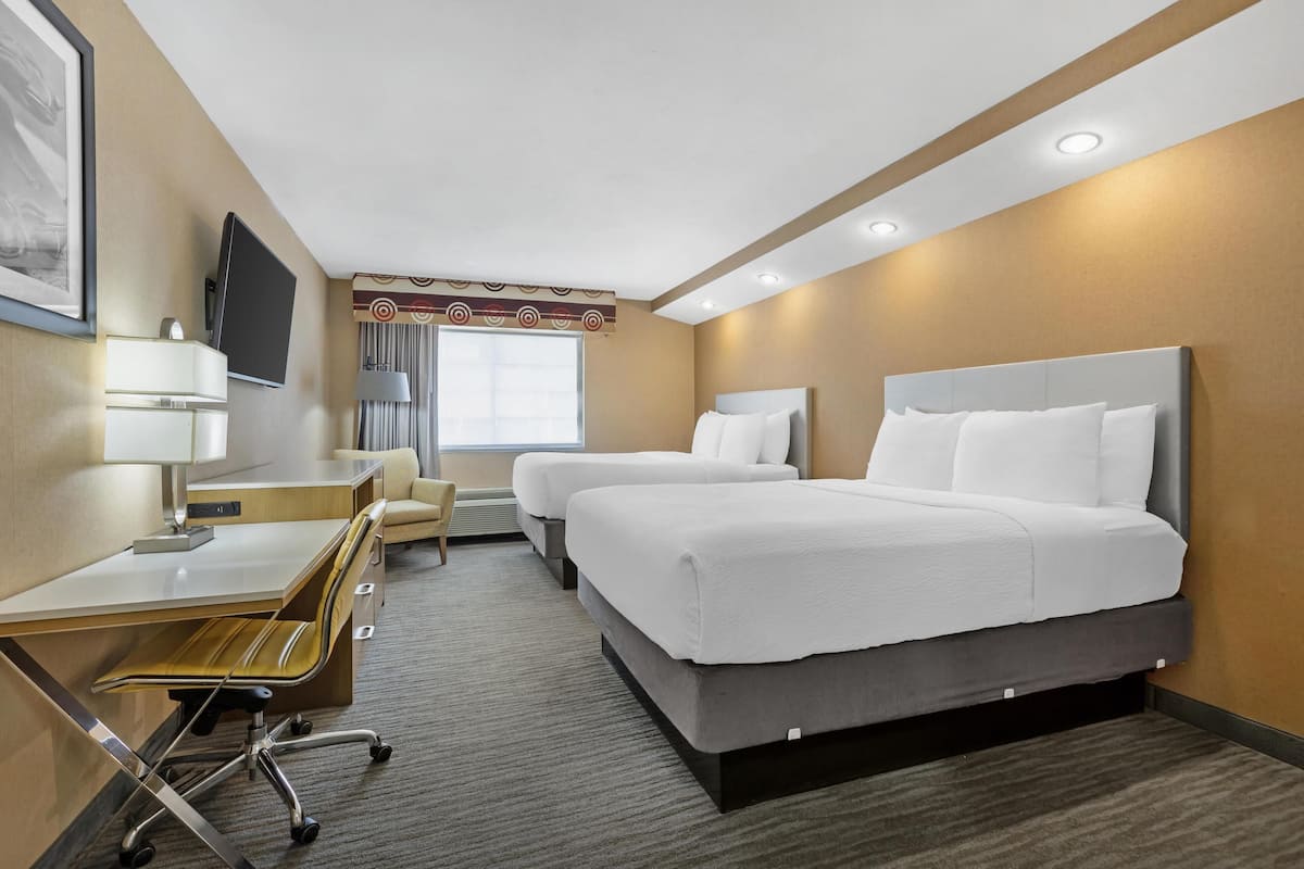A hotel room with a desk, two beds, a TV, and a window.