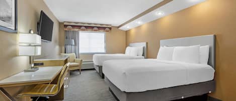 A hotel room with a desk, two beds, a TV, and a window.