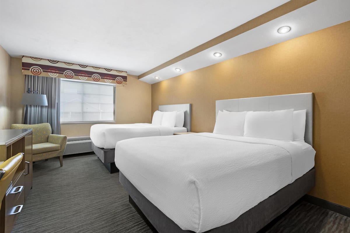 A hotel room with two beds, a desk, and a chair.
