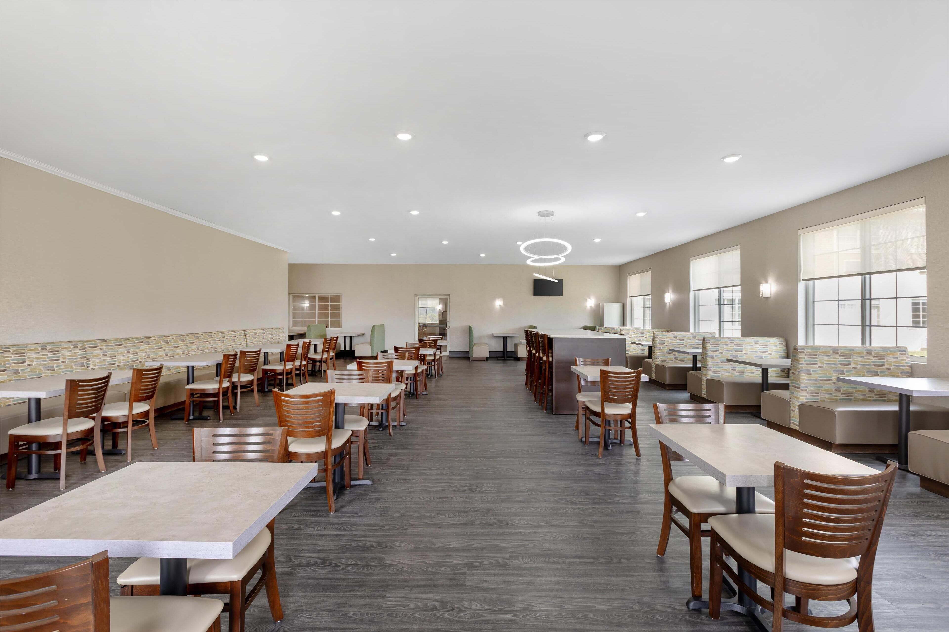 A spacious indoor dining area with multiple tables and booths, a central counter, and large windows providing natural light.