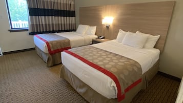 Habitación de hotel con dos camas, una ventana con cortinas, una lámpara fijada a la pared y un suelo estampado.